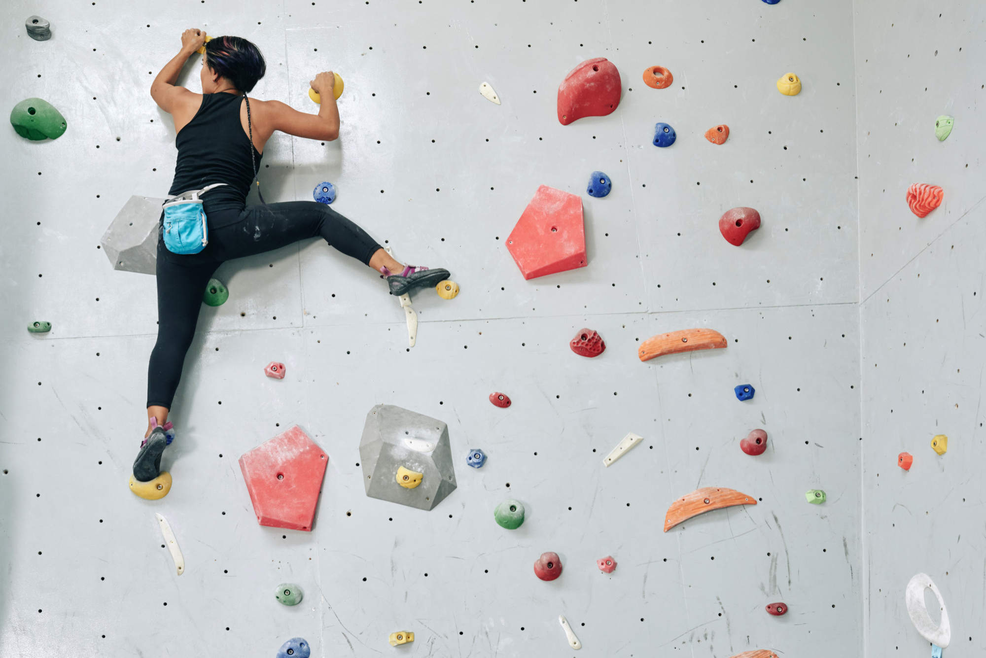 Grimpeuse sur un mur d’escalade intérieur équipé de prises et de volumes colorés