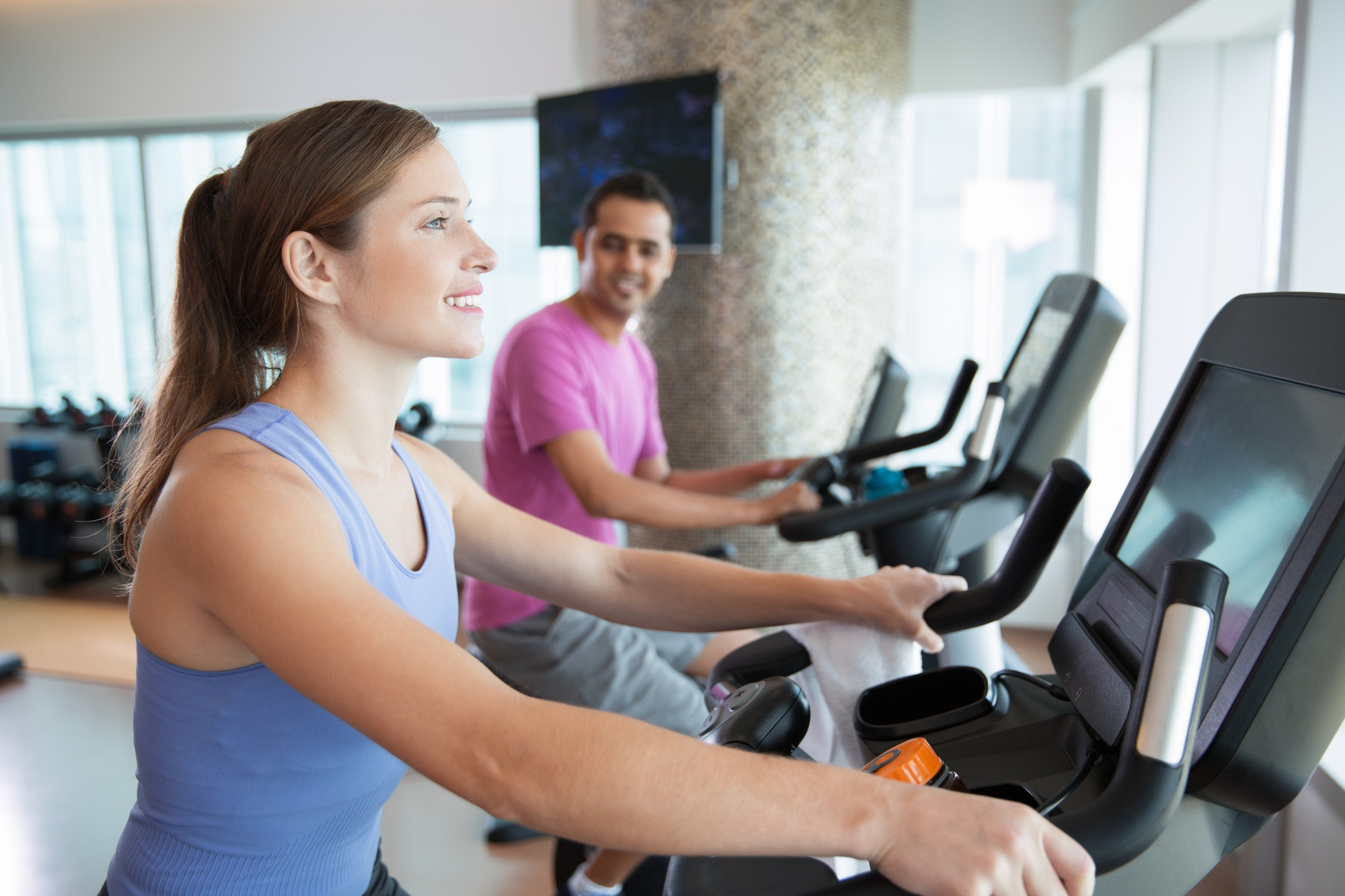 Deux personnes s’entraînent sur des appareils de cardio dans une salle de fitness